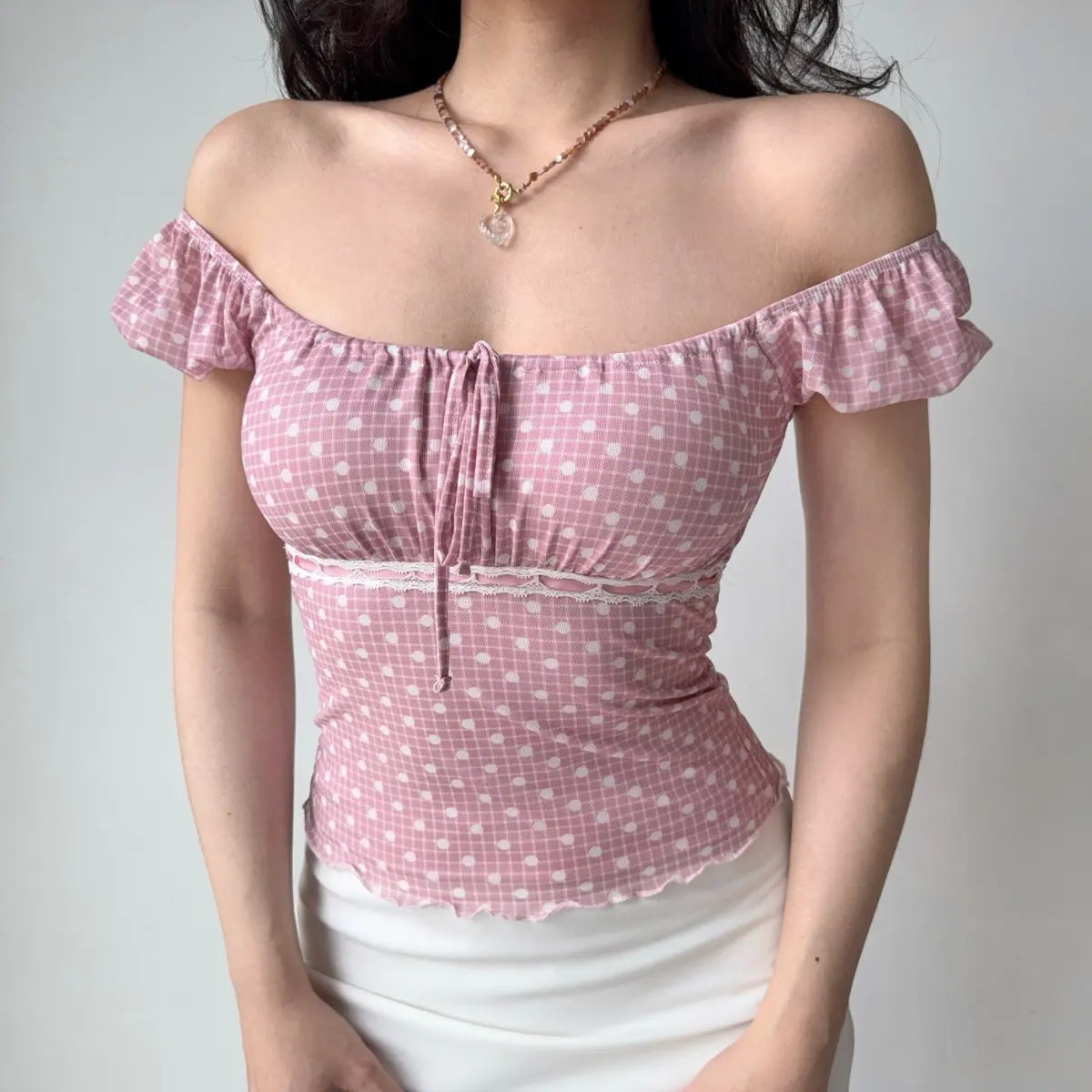 Model wearing pink-white polka-dot top styled as off-the-shoulder, with ruffled sleeves, lace trim and front tie detail