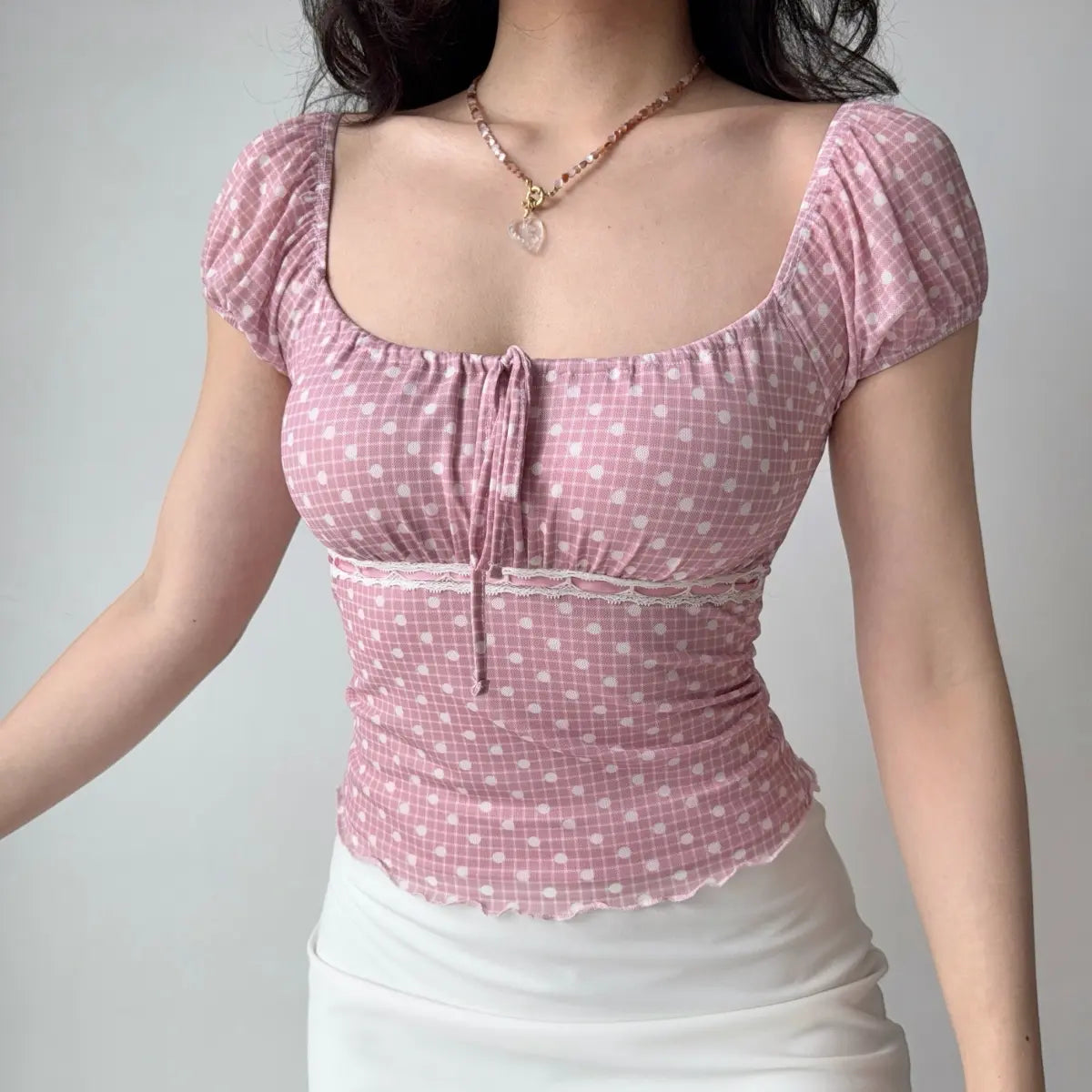 Model wearing pink-white polka-dot top with square neckline, puff sleeves, front tie detail and lace trim, fitted mesh blouse