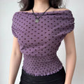 Model wearing purple polka-dot off-the-shoulder top with smocked waist and ruffled hem, front view showing silhouette and pattern