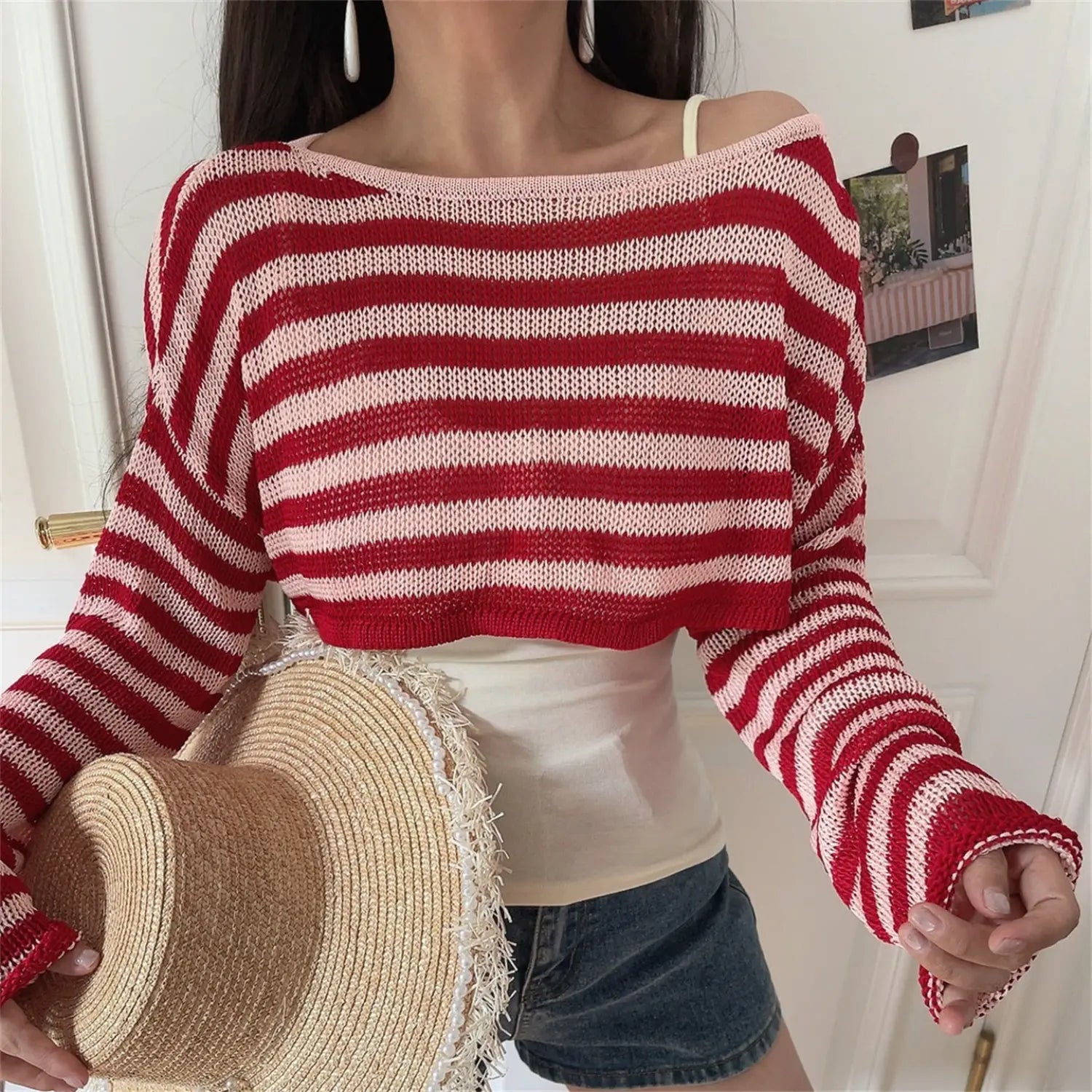 Slightly side front view of loose mesh knit striped top, off shoulder sloped neck, cropped hem with denim shorts