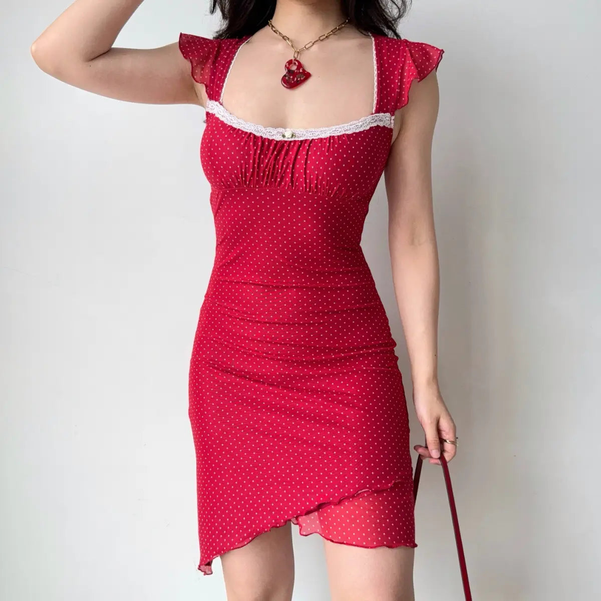 Model wearing red polka dot mesh mini dress with ruffled shoulder straps, sweetheart neckline and asymmetrical hem