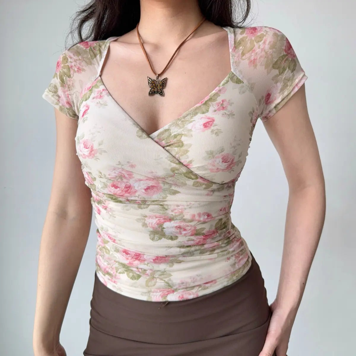 Model wearing rose-print sheer mesh wrap-style top with short sleeves, deep V-neckline and form-fitting silhouette