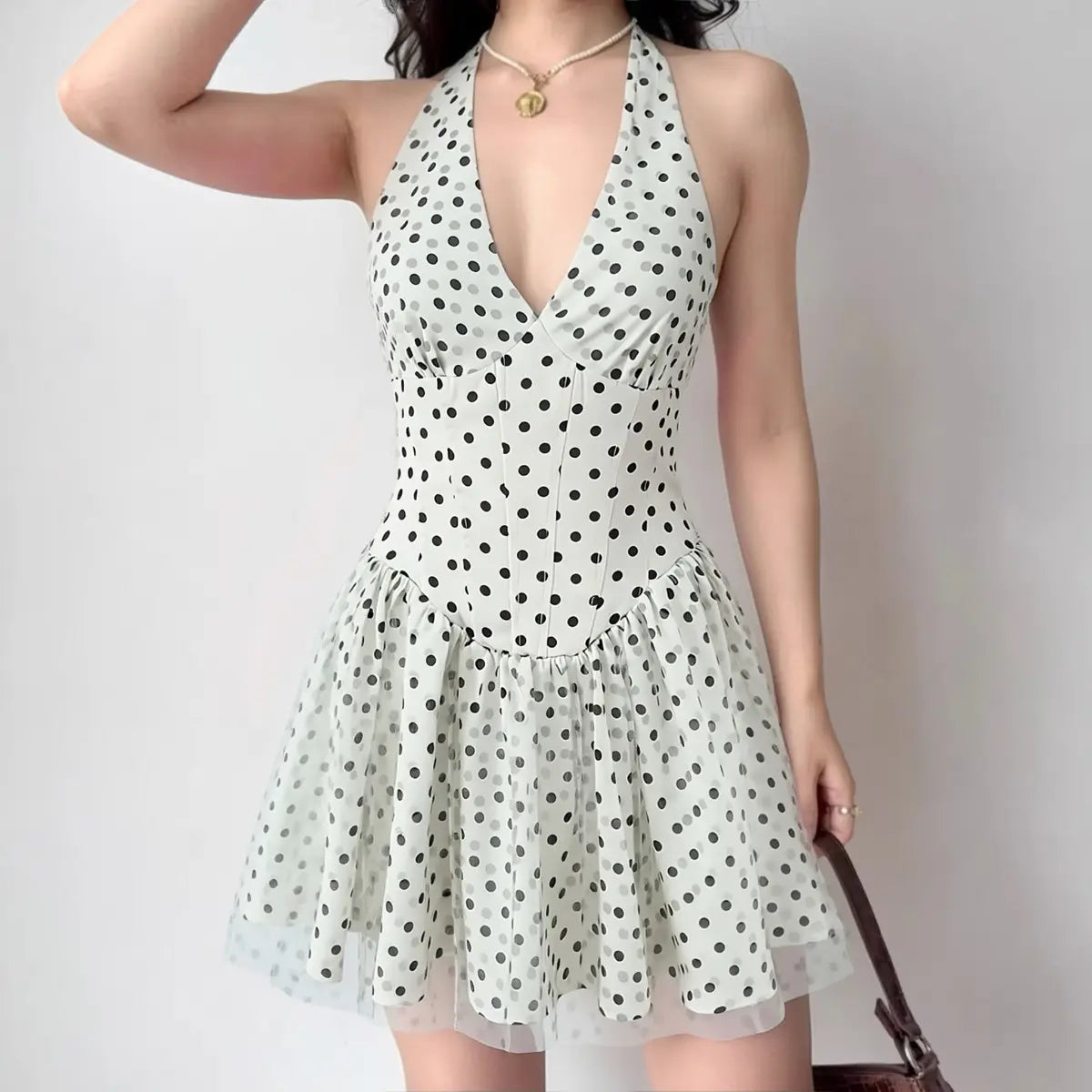 Model wearing white with black polka dot halter mini dress, front view