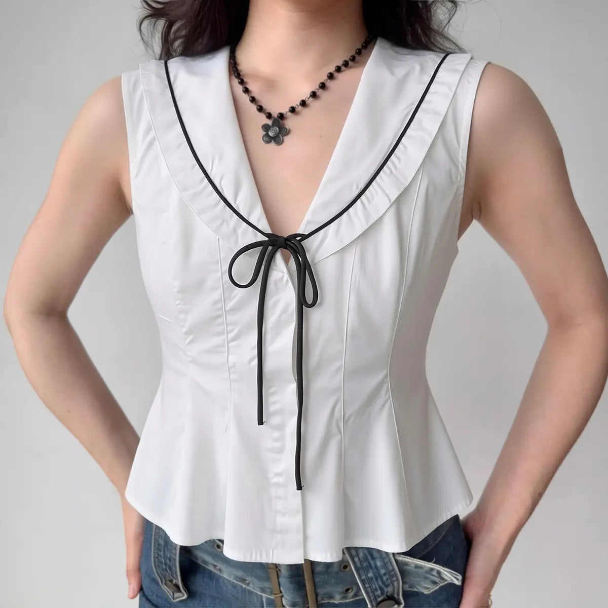 Model wearing white black-trim tie-front peplum vest top, preppy-inspired fitted sleeveless blouse