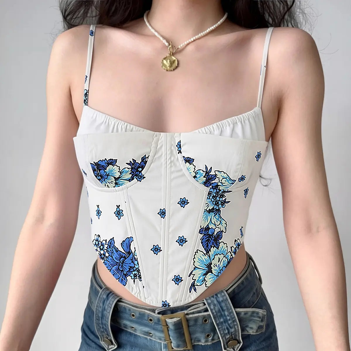 Model wearing white and blue floral corset cami top with thin straps, styled with jeans