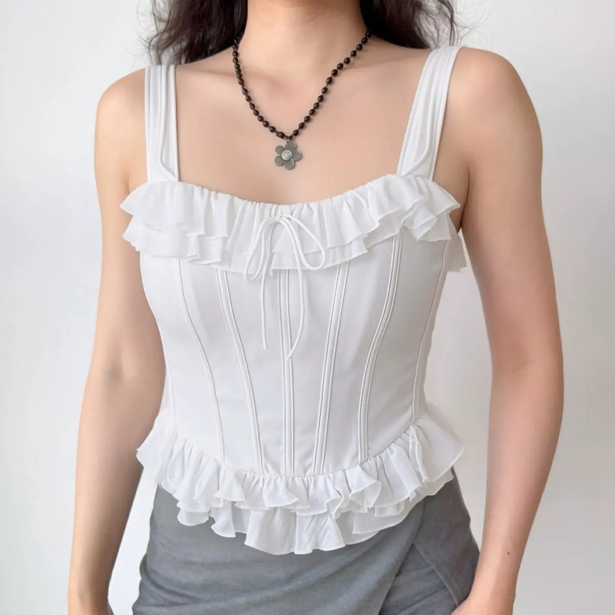 Model wearing white corset-style cami top with ruffled trim and structured boning