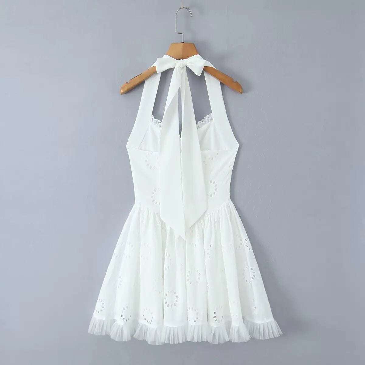 White eyelet halter dress hanging on wooden hanger, back view showing tie closure