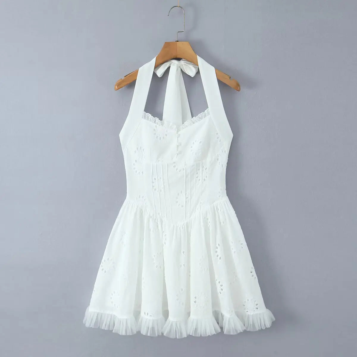 White eyelet halter dress hanging on wooden hanger, front view