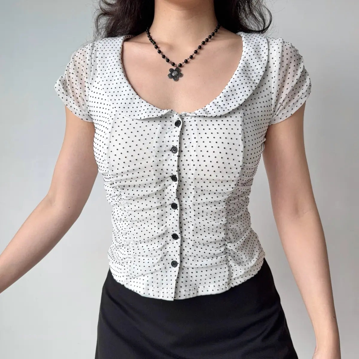 Model wearing white eyelet lace top with Peter Pan collar, puff short sleeves, button-down front, and ruched side detailing