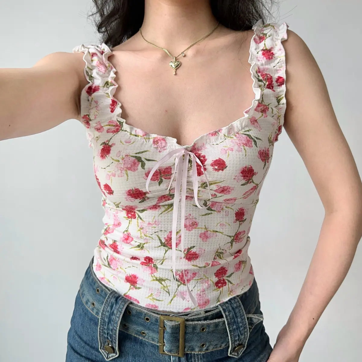 Model wearing white floral print cami top with ruffled scallop straps, sweetheart neckline, front tie detail, and form-fitting cropped silhouette