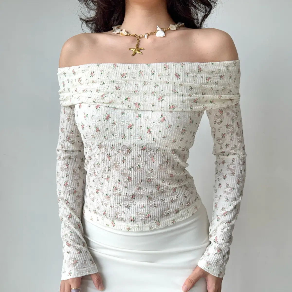 Model wearing white floral-print off-the-shoulder top with textured ribbed fabric and lace detail, fitted long-sleeve blouse