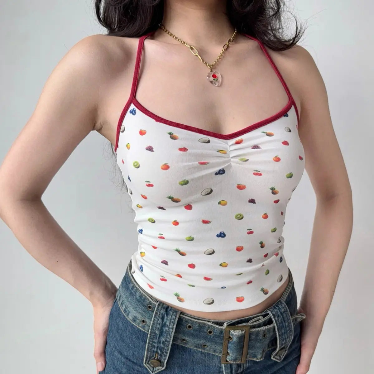 Model wearing white fruit-print halter-neck cami top, front view showing red trim, print and ruched bust detail