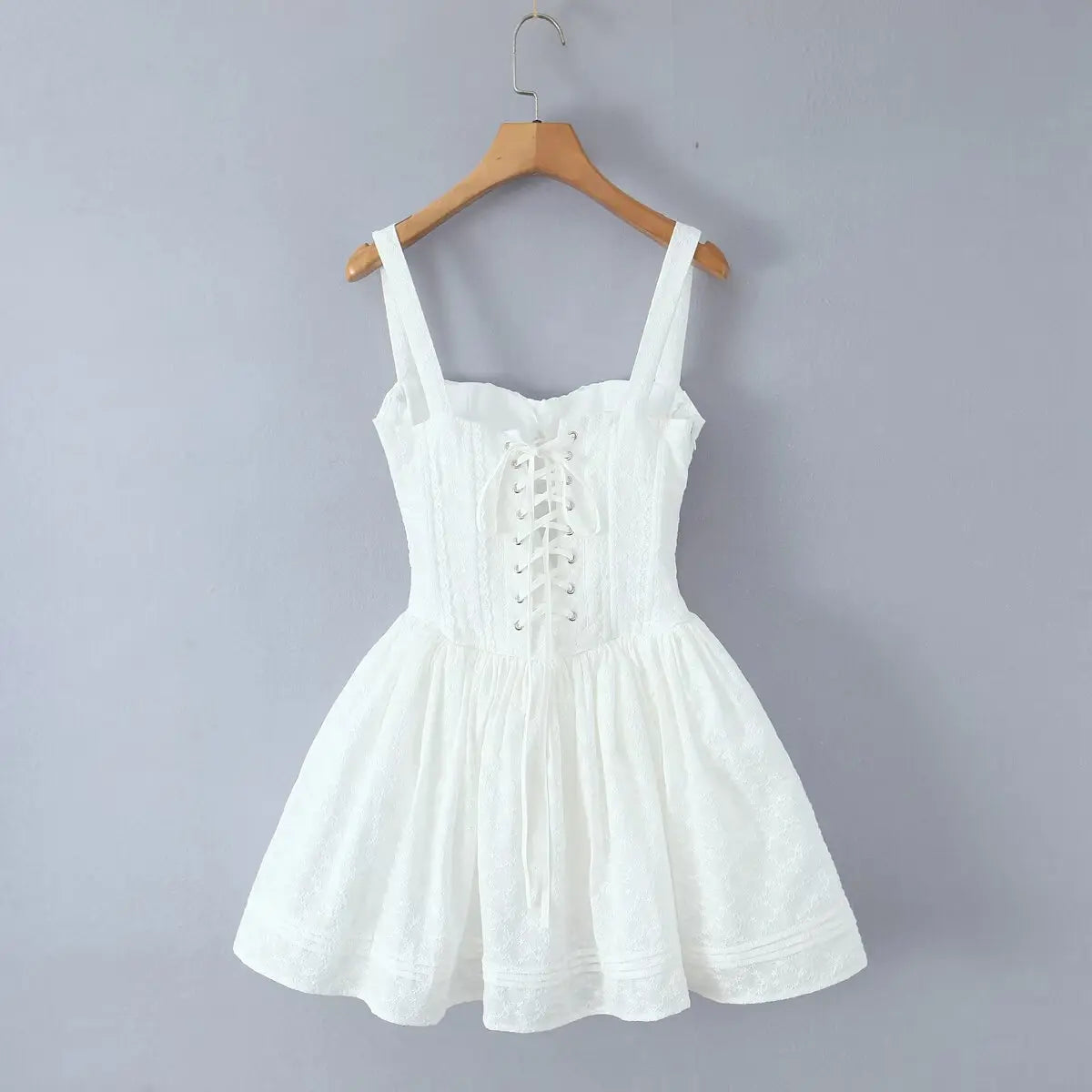 White lace cami dress with lace-up back hanging on wooden hanger, back view