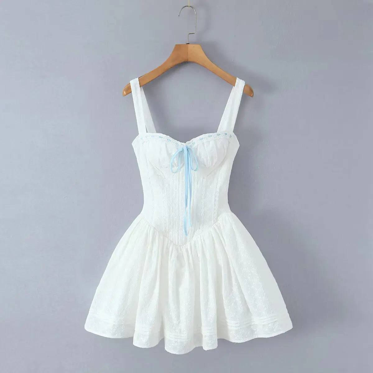 White lace cami dress with blue ribbon hanging on wooden hanger, front view