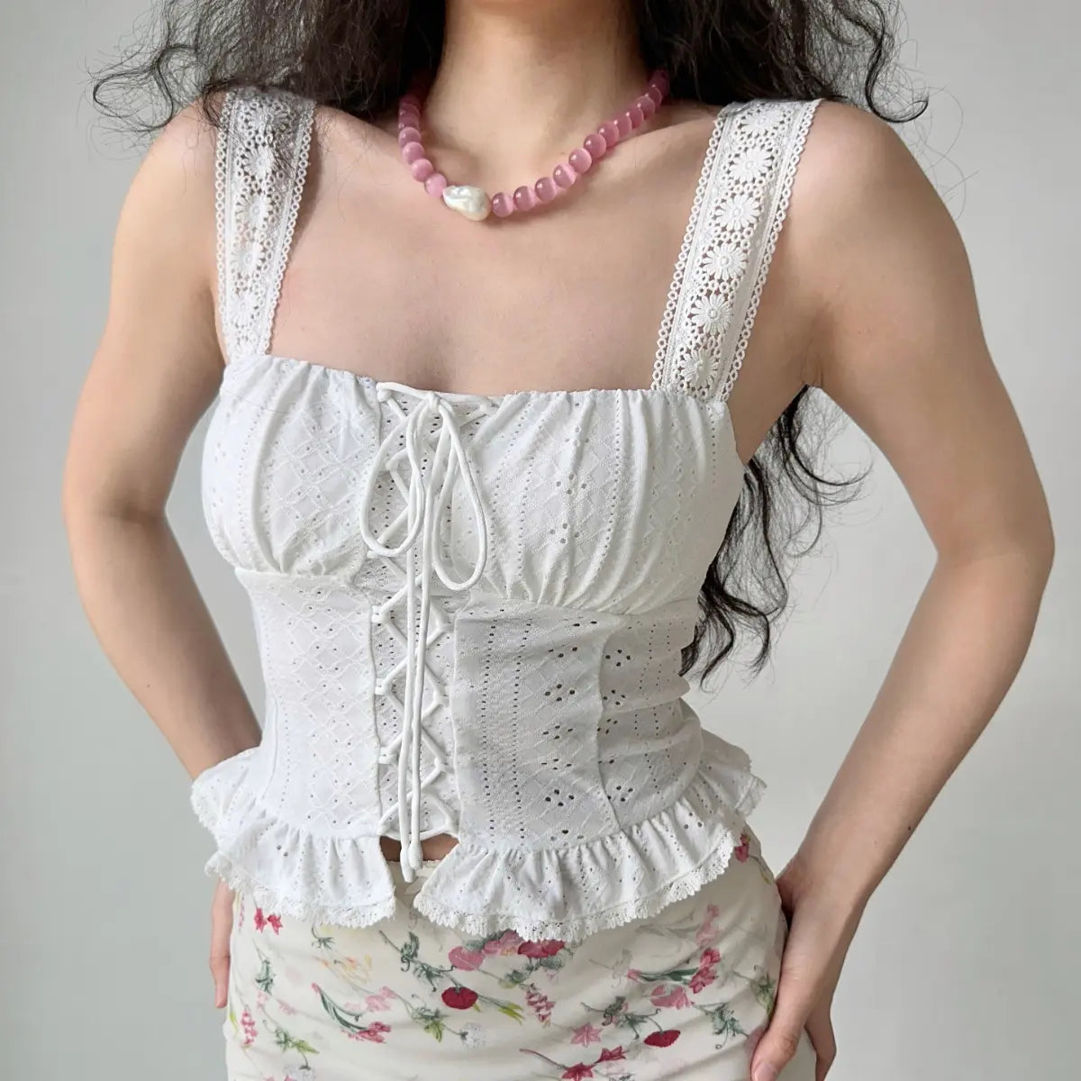 Close-up front view of model wearing white lace eyelet lace-up cami top