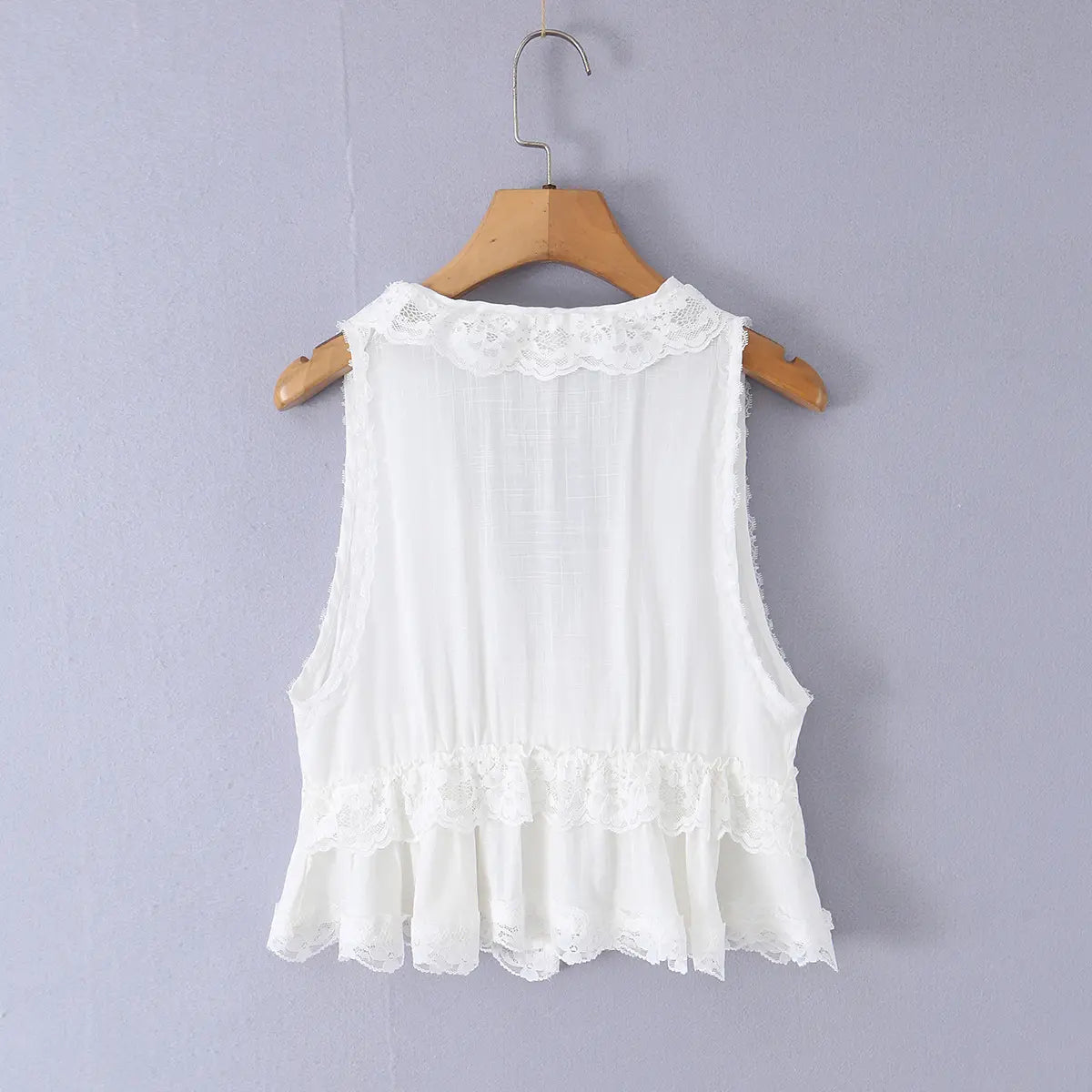 White lace sleeveless top hanging on wooden hanger, back view showing ruffled hem