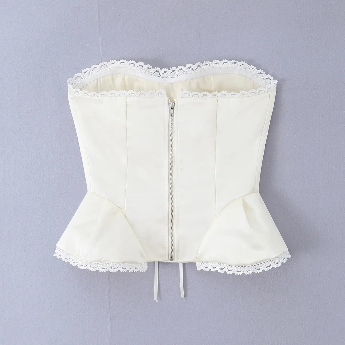 Hanger back view of white satin corset top with zipper closure and lace-trimmed peplum hem