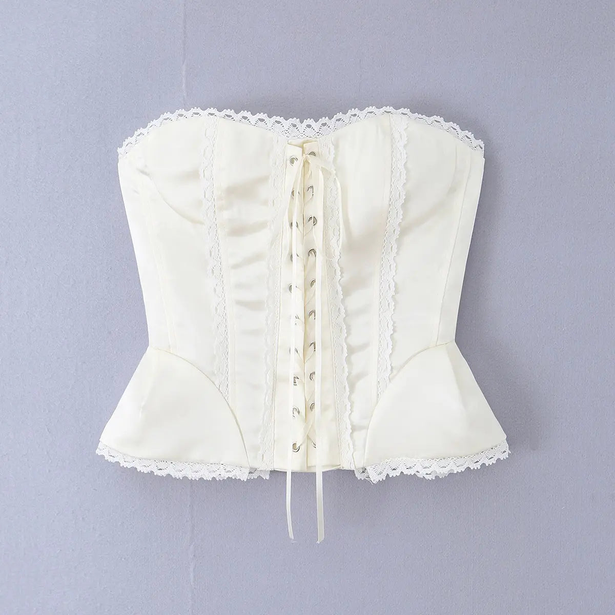 Hanger view of white satin corset top showing front lace-up closure, lace trim, and peplum hem
