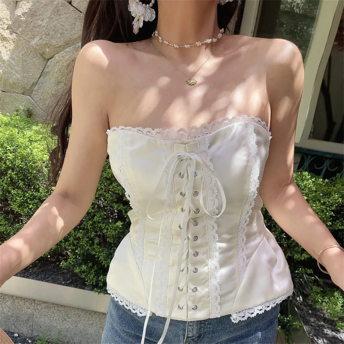 Model wearing white satin strapless corset top with lace trim, front lace-up closure, and peplum hem