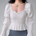 Model wearing white square-neck puff-sleeve blouse with smocked waist and peplum hem, feminine vintage-inspired top