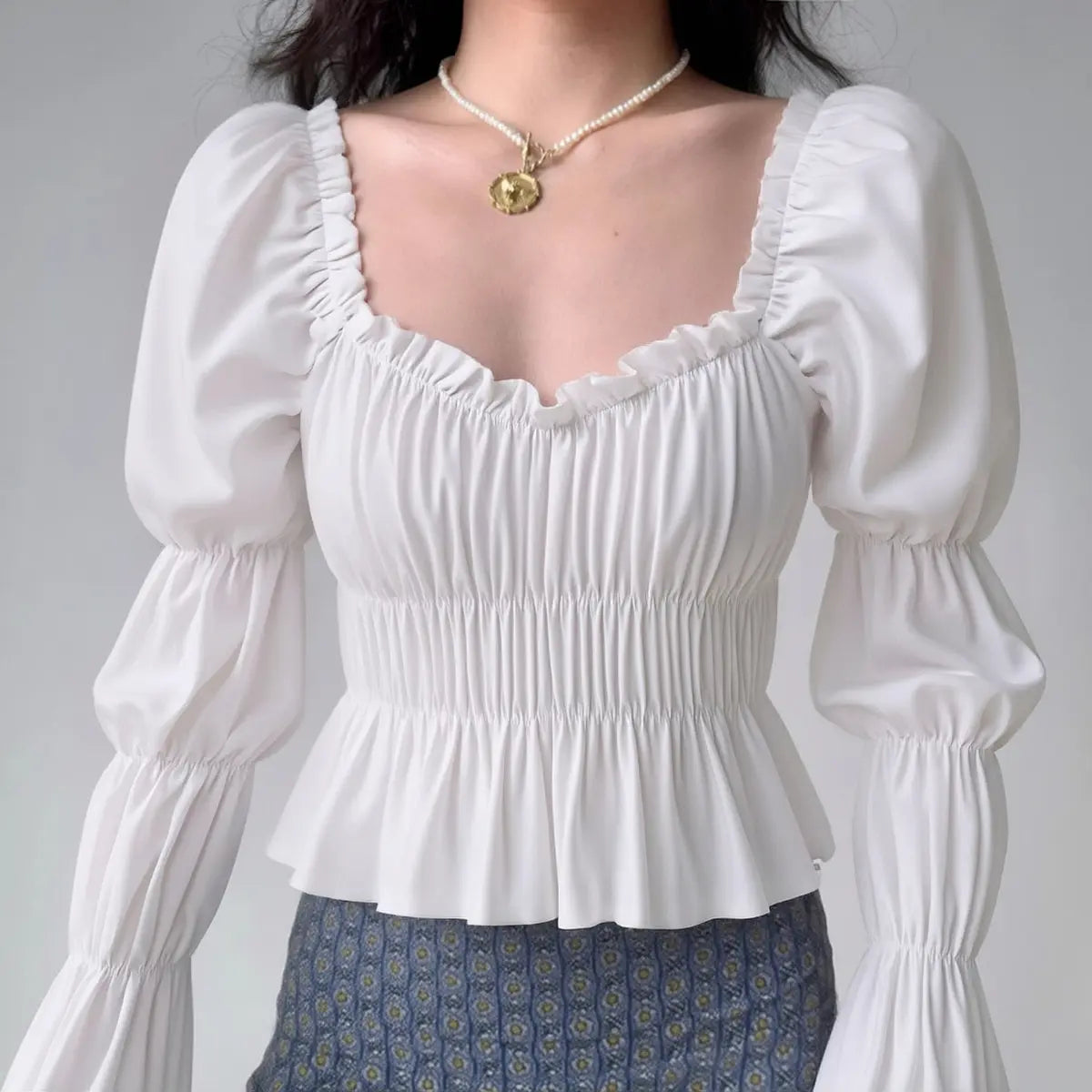 Model wearing white square-neck puff-sleeve blouse with smocked waist and peplum hem, feminine vintage-inspired top