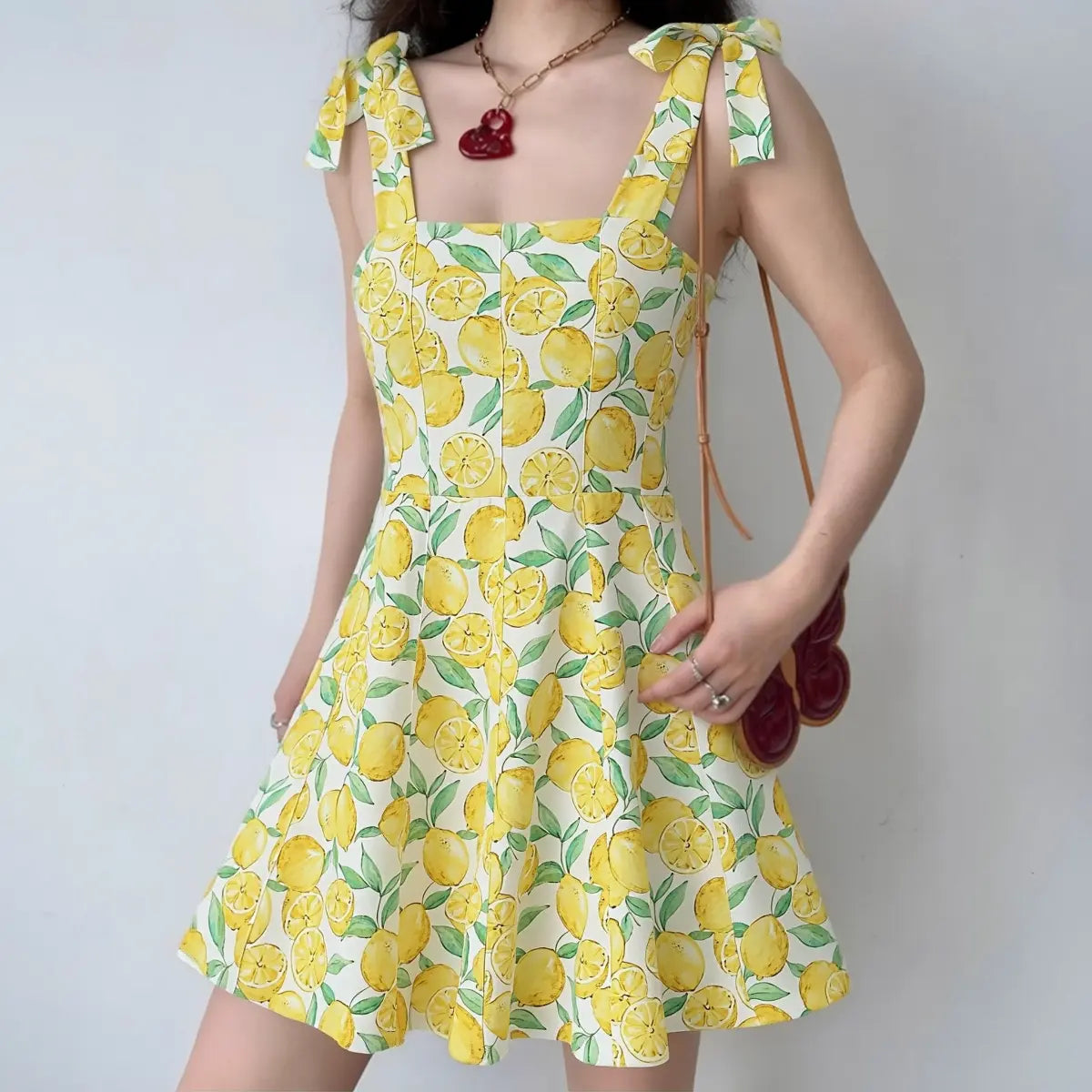 Model wearing yellow lemon print cami mini dress with bow-tie straps, square neckline and flared skirt