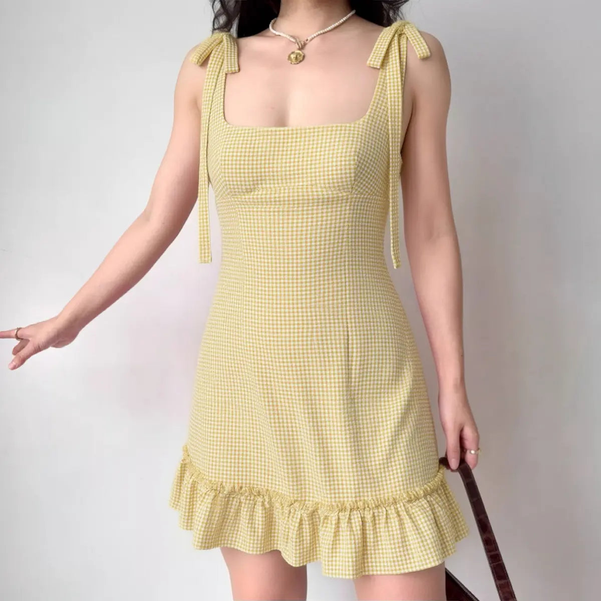 Model wearing yellow white gingham dress with tie straps and ruffle hem, summery A-line mini dress