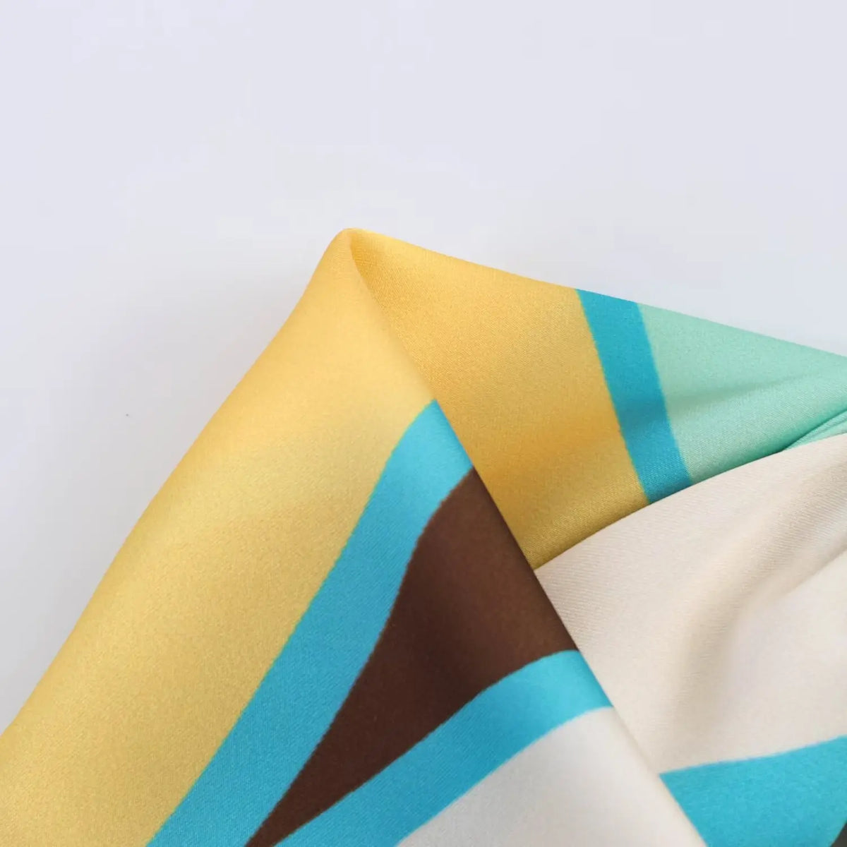 Macro close‑up of abstract geometric print satin fabric, yellow turquoise brown pattern