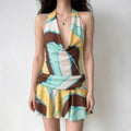 Woman model wearing abstract geometric print halter mini dress, cowl neck, ruffle hem, plain wall background