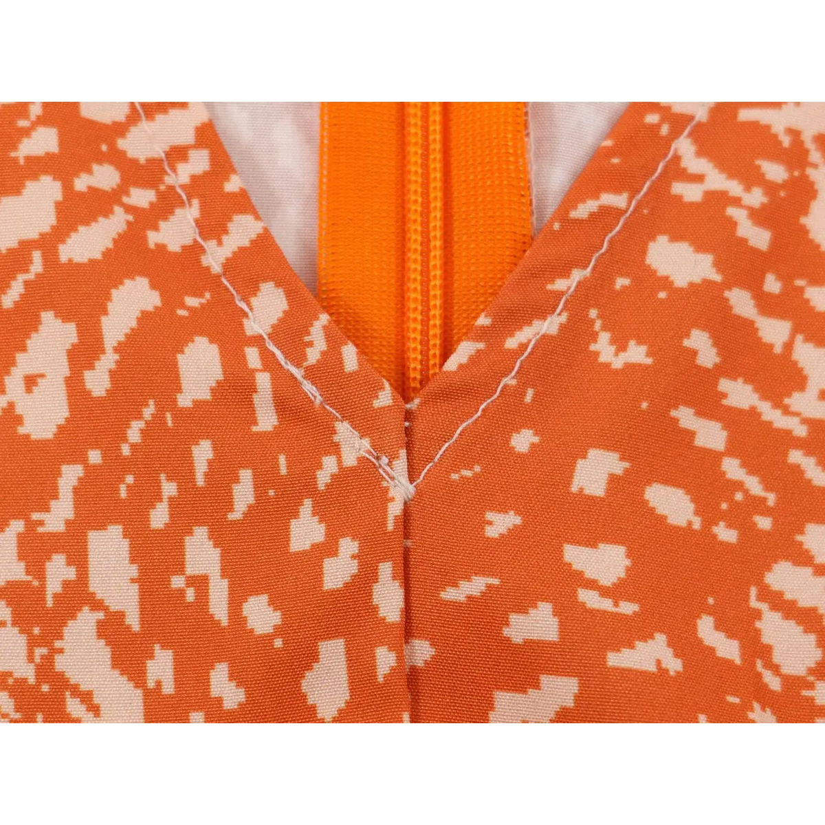 Close-up of v neck stitching and front zipper construction on orange abstract print maxi dress