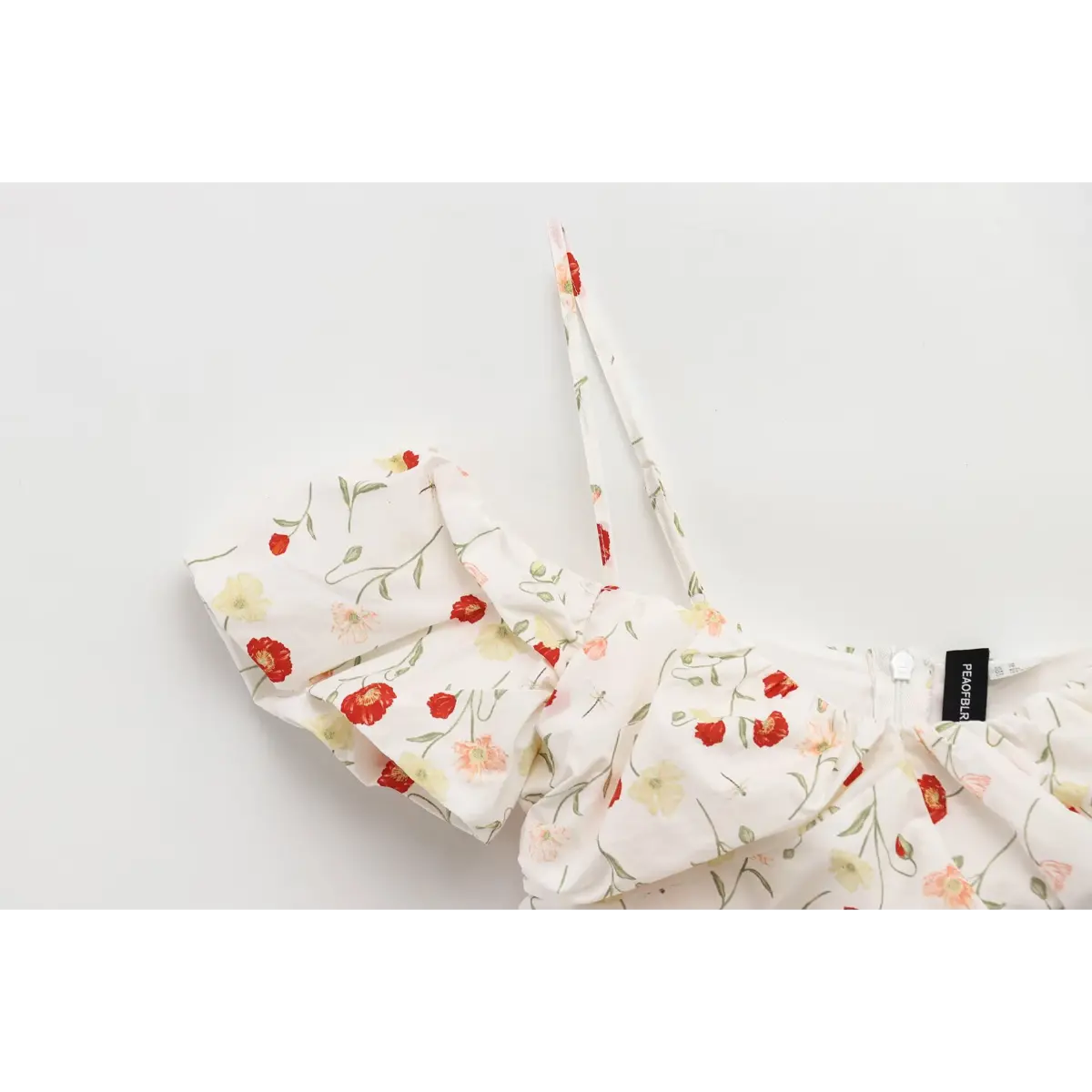 Close-up of the adjustable spaghetti strap on a white poppy-print dress, showing the strap with matching floral print.