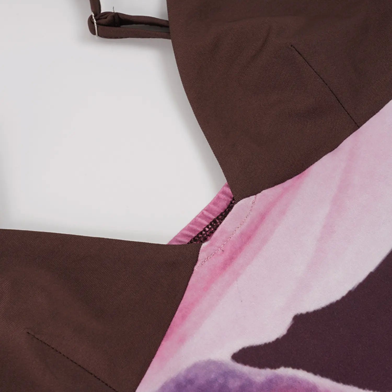Top-down partial close shot of slip dress V-neck construction, adjustable slider thin brown straps, neat zigzag seam connecting solid brown bust panel to printed magnolia skirt fabric