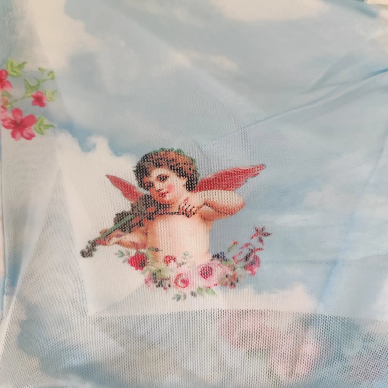 Close‑up cherub angel and rose artwork print on light blue sheer mesh fabric