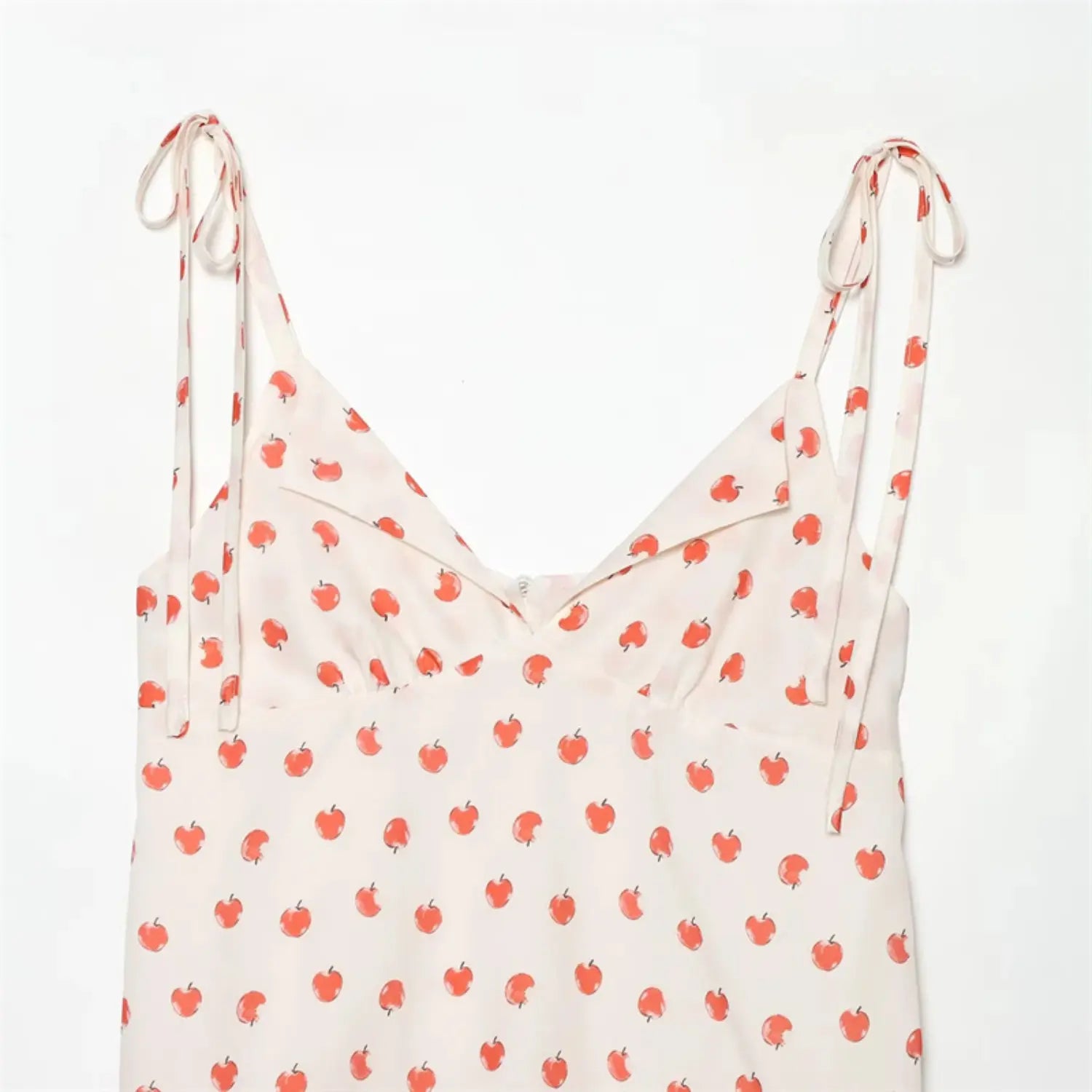 Closeup front V neck full view, self-fabric tie spaghetti straps, folded lapel V neck, all-over red apple print on cream base, hidden side zipper, lightweight soft woven fabric