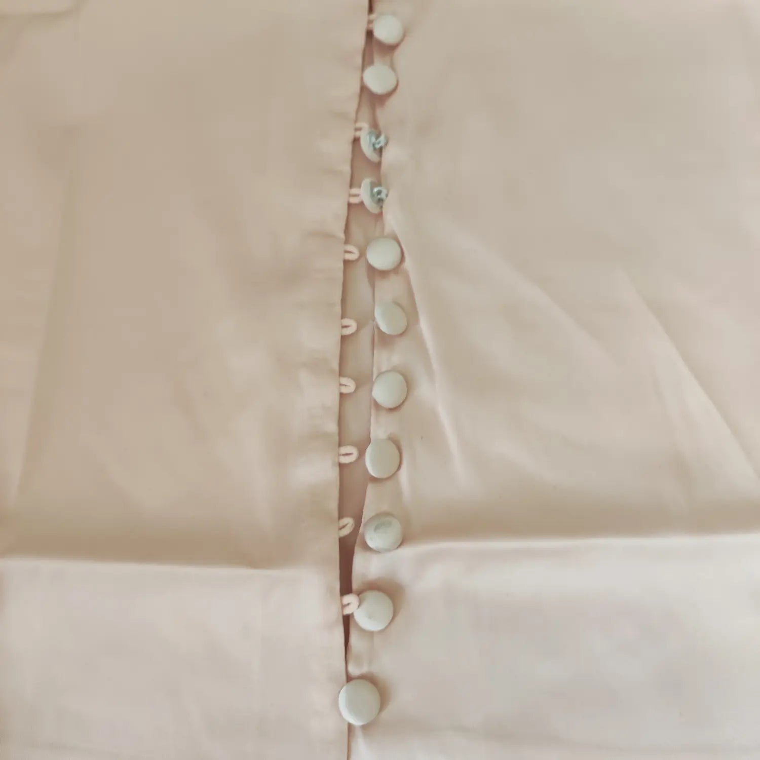 Close‑up of fabric covered buttons and button loop placket on apricot pink satin cami top