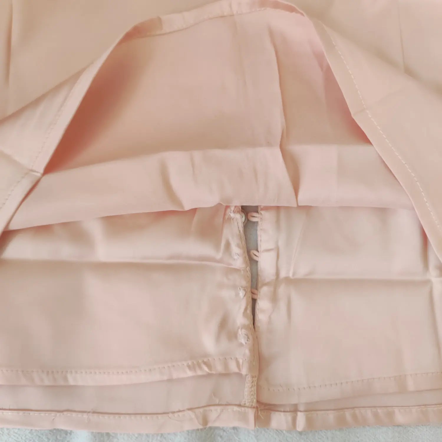 Close‑up inner view of front button placket and lining stitching on apricot pink satin cami