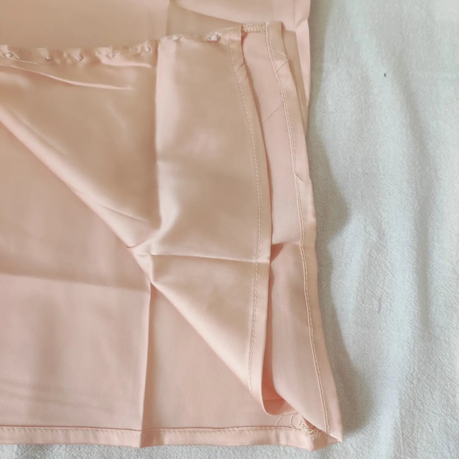 Close‑up side seam and hem stitching detail apricot pink satin camisole top