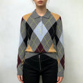 Model wearing grey argyle knit sweater with black trousers on white background