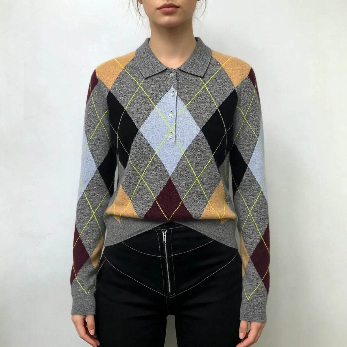 Model wearing grey argyle knit sweater with black trousers on white background