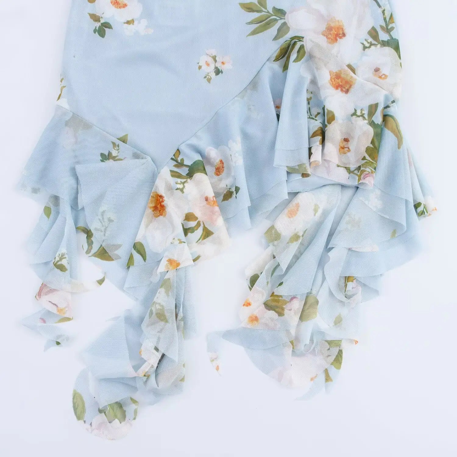 Close‑up of asymmetrical jagged ruffle hem with long hanging streamers, light blue mesh fabric with white floral print