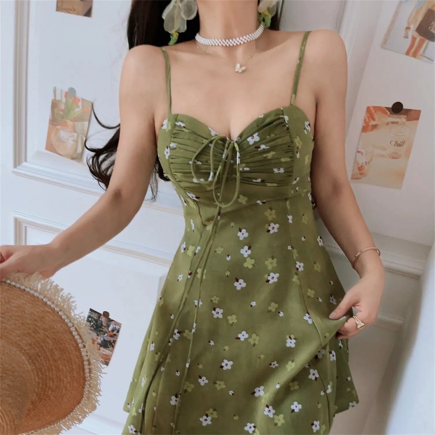Avocado green tiny floral drawstring cami mini dress half body shot, v-neck gathered bust a-line skirt, model with pearl frayed straw hat korean soft indoor styling