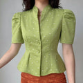 Daily front lifestyle shot of avocado green polka dot satin blouse, split stand collar, puff short sleeves, two matching fabric covered buttons, waist dart peplum slim silhouette, matched with orange textured bottoms, vintage gentle daily styling