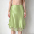 Model wearing avocado green satin midi skirt, high waist, textured shiny satin fabric, double layered hem, flowy A-line silhouette, plain white background
