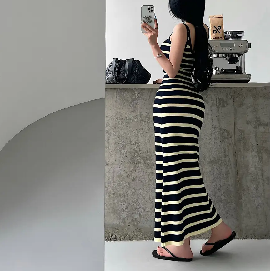 A woman wearing a navy and pale yellow striped ribbed knit maxi dress, showing the back view and form-fitting silhouette.
