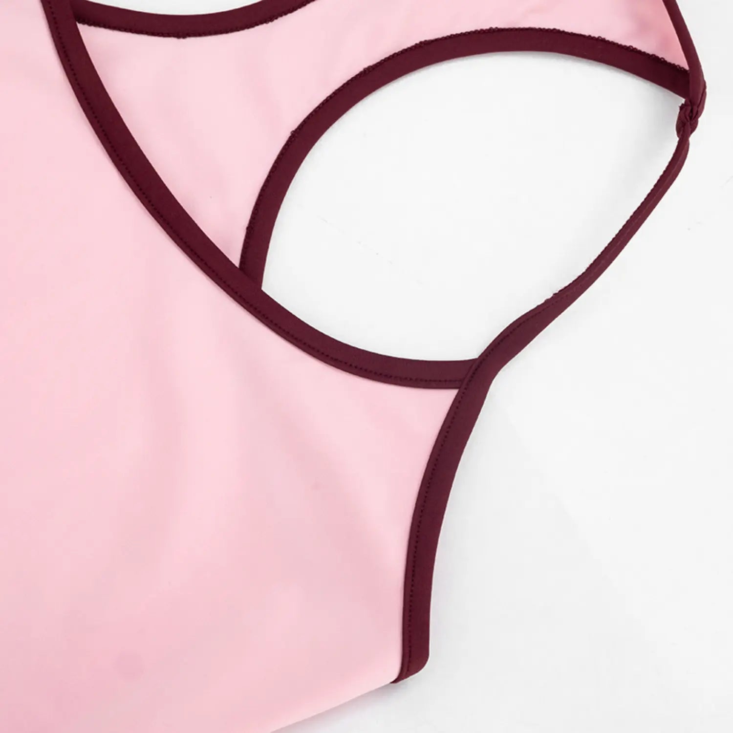 Macro close shot of halter tank top back cutout detail, soft baby pink stretch fabric with thin burgundy contrast binding, neat uniform overlock stitching along all edge trim, slim thin halter straps