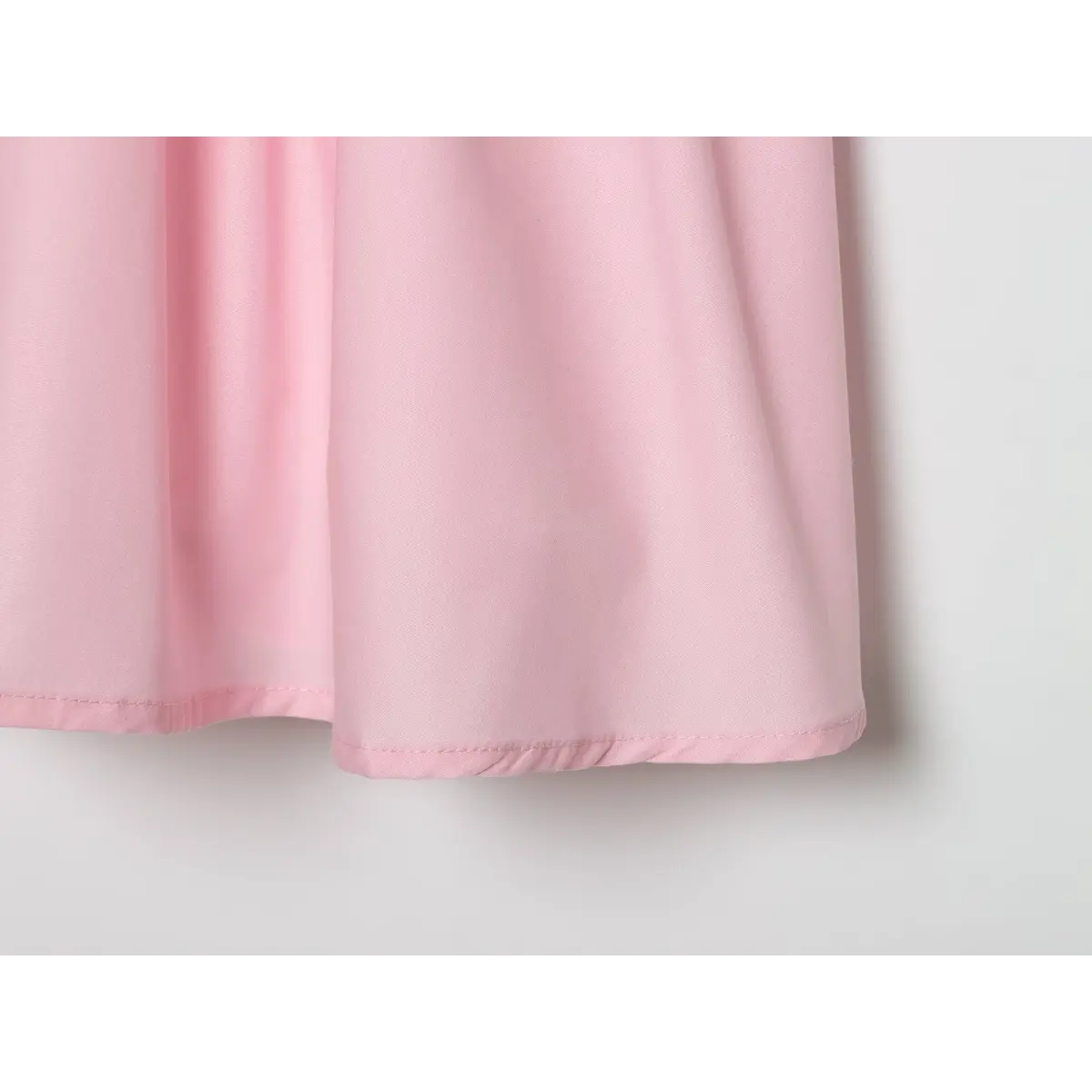Close-up hem detail of blush pink sleeveless mini dress, neat folded finished stitching on solid soft woven fabric.