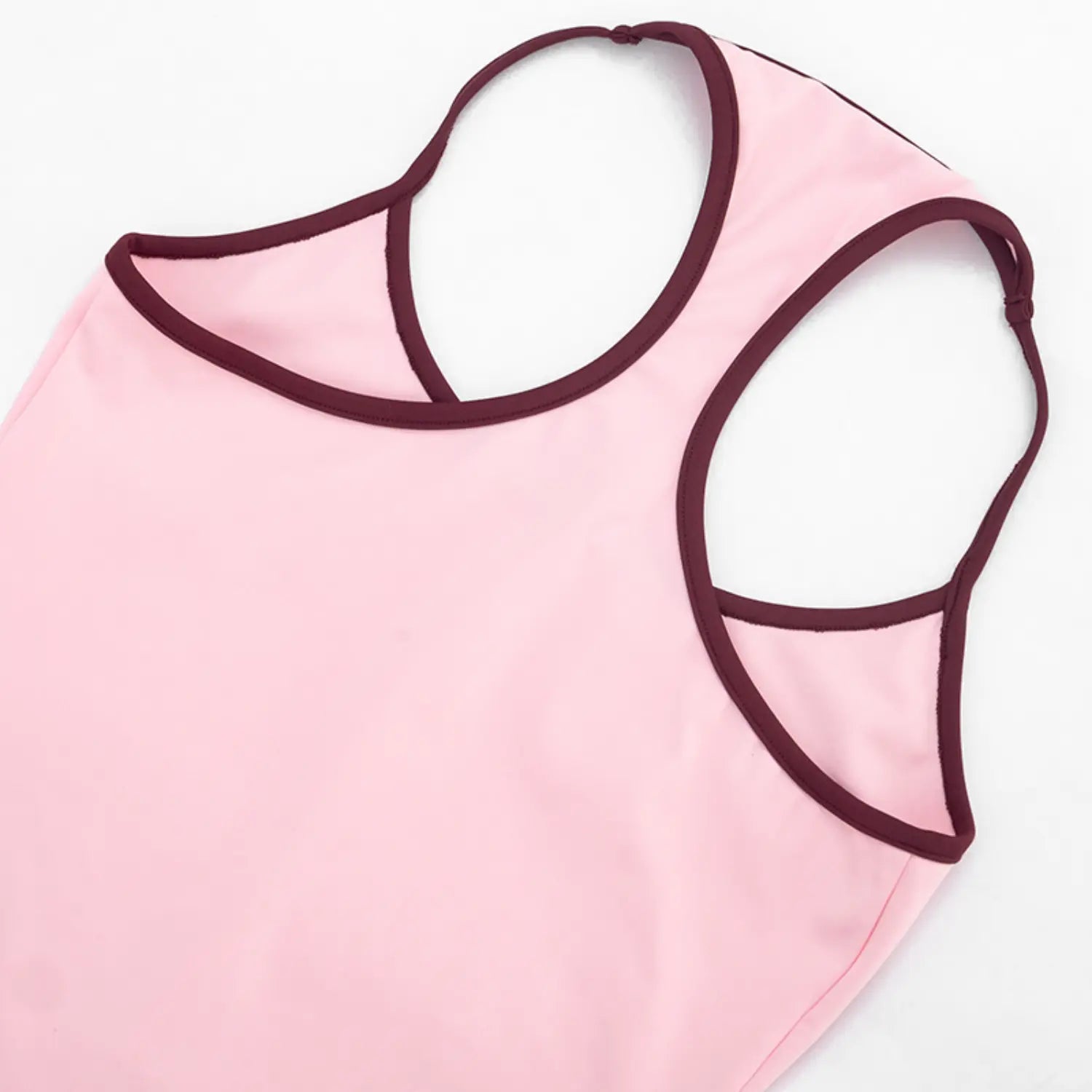 Top-down partial shot of dual thin halter straps with burgundy contrast binding, large curved rear racer cutout, solid light pink stretch fabric with wrinkle-resistant soft texture