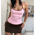 Relaxed daily wear indoor bedroom shot of soft pink stretch halter tank top with burgundy neck contrast piping, subtle side waist ruching for figure shaping, matched with ruched dark brown mini skirt, stackable shell bracelets, plain white wall and bookshelf backdrop