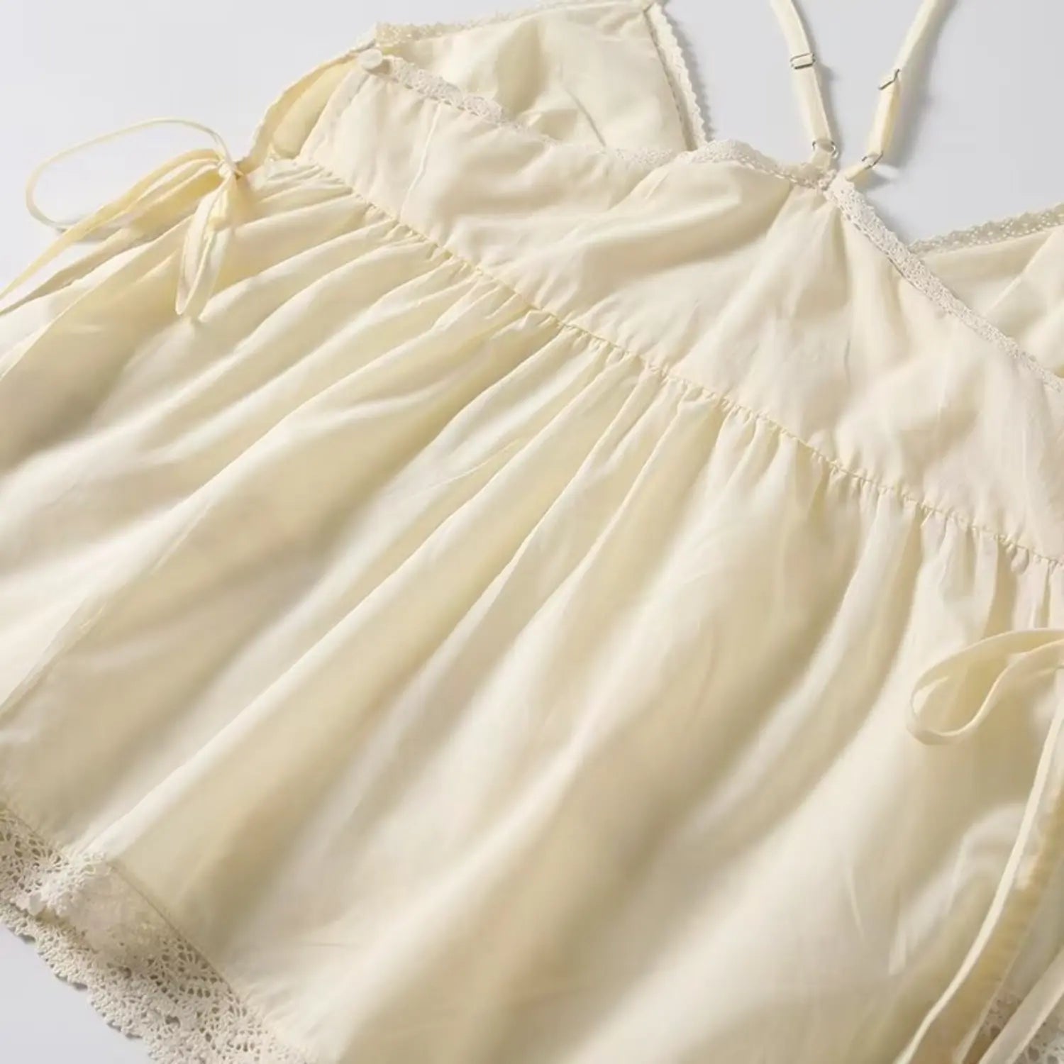 Angled view of cream babydoll cami top, loose gathered hem, side drawstring and scalloped lace