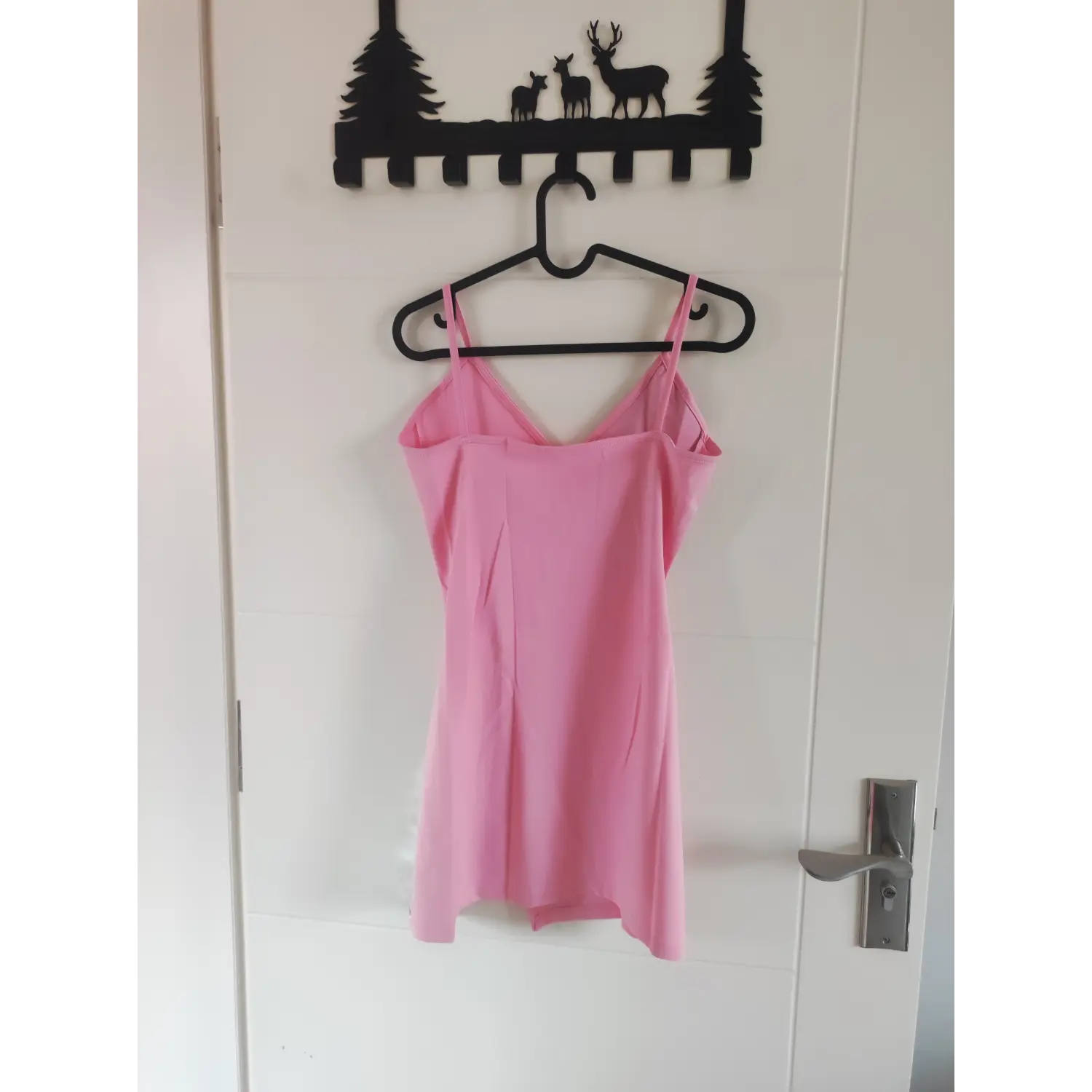 Back hanging view pink stretch spaghetti strap mini dress displayed on hanger against white door